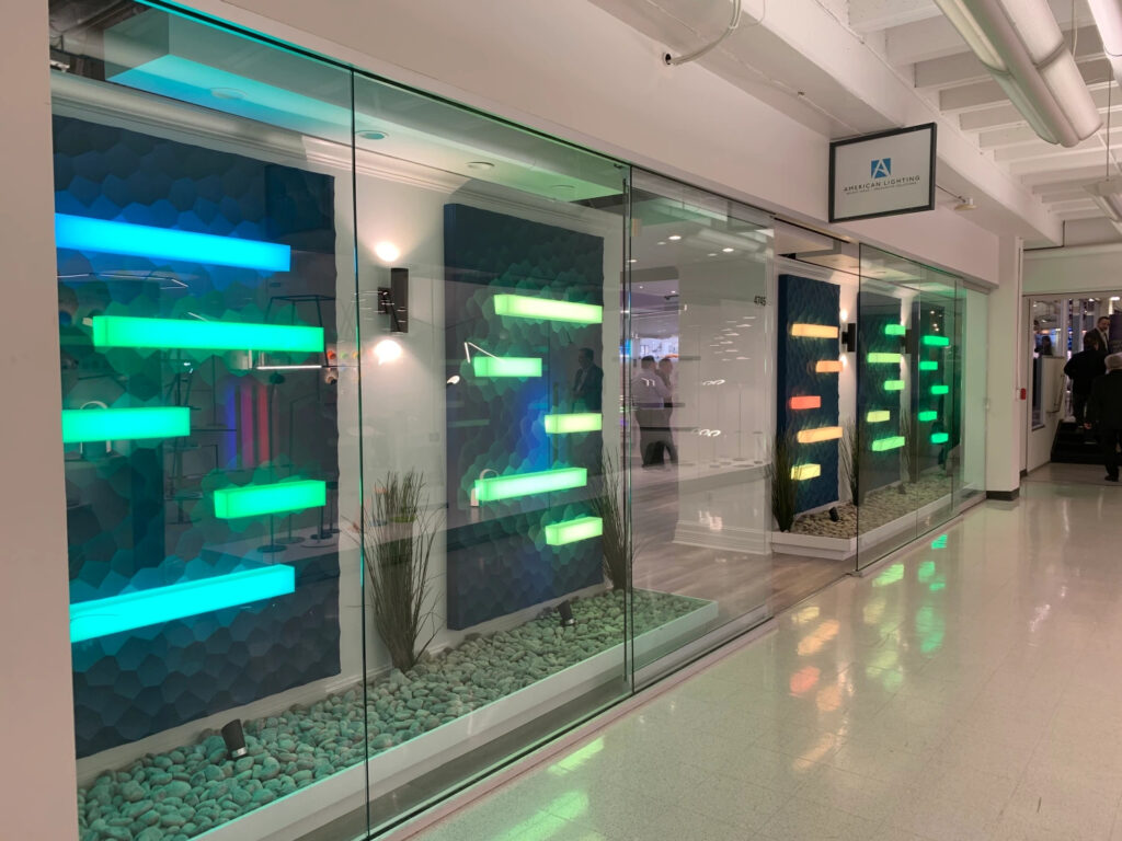 The American Lighting display area that includes a glass display wall with rectangles of various colored lights at different heights and with different widths and a doorway in the middle