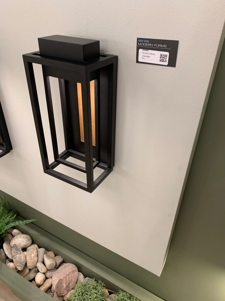A large black rectangular outdoor light fixture with a copper back and a light source concealed in the top hanging on display