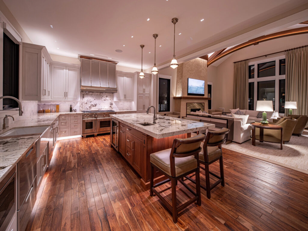 A fancy, expensive, modern kitchen with marble countertops and island and wooden floors, opening into a large fancy modern living room