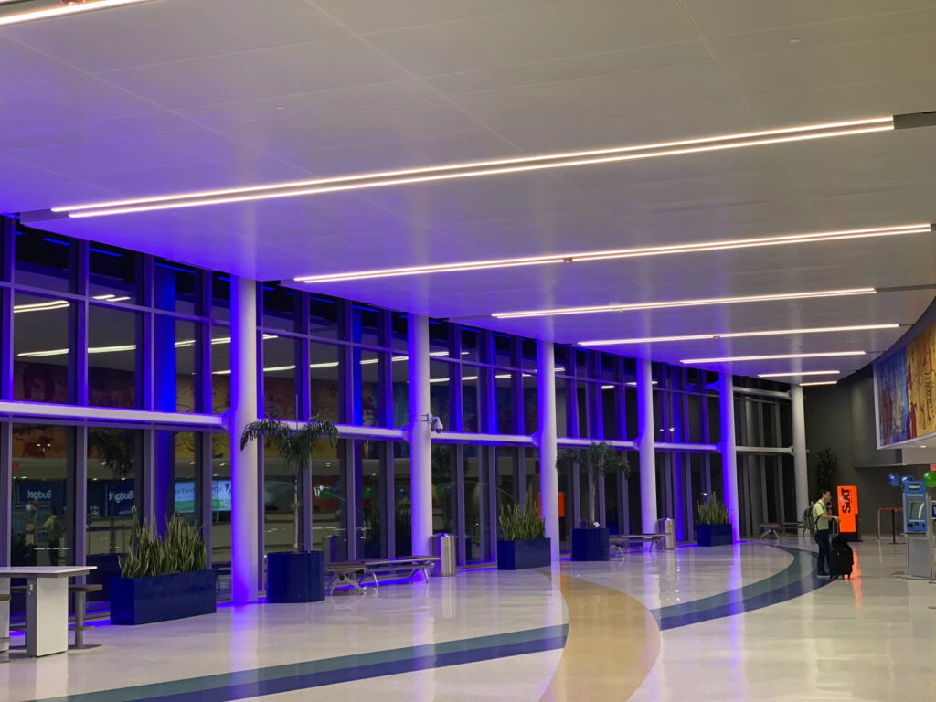 The lobby at an airport where a large bank of windows are lit with indigo lights