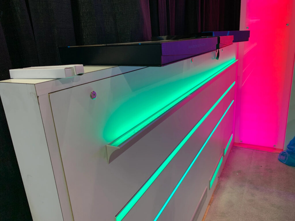 A half wall with green light strips along the length of it next to a wall lit up in pink