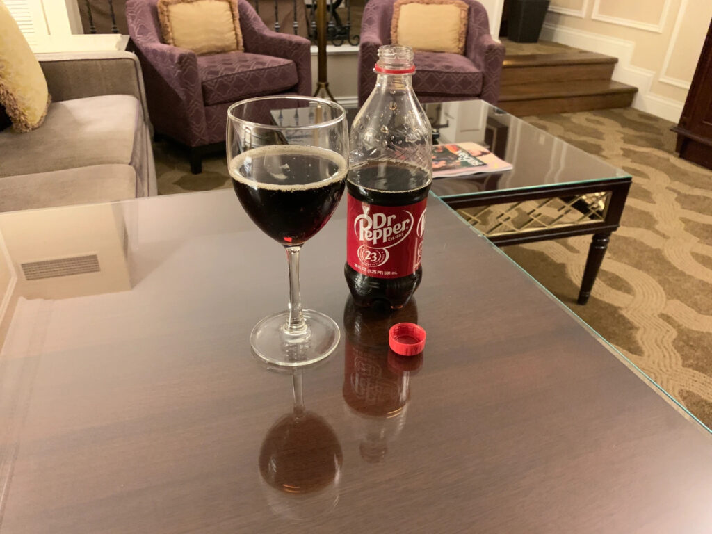 A wine glass half filled with a bottle of Dr. Pepper next to it atop a coffee table