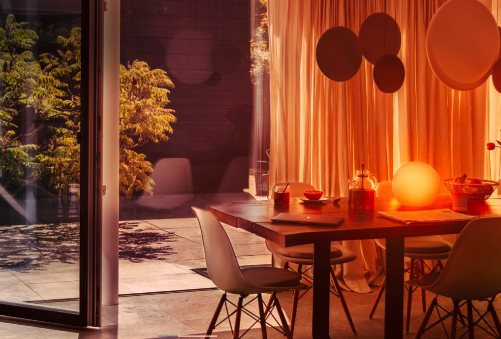 An outdoor table and chairs in front of a curtain with circular pendants hanging above it and a globe light atop the table lighting the area up with orange light.