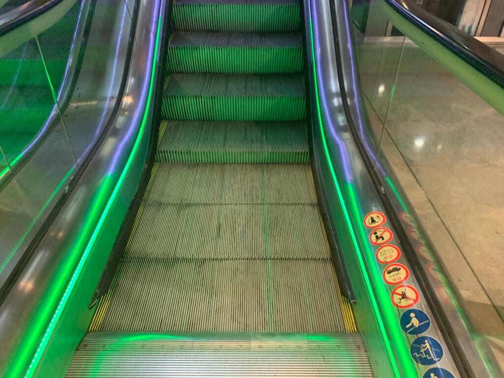 The entrance to an up escalator is lit up with green lights