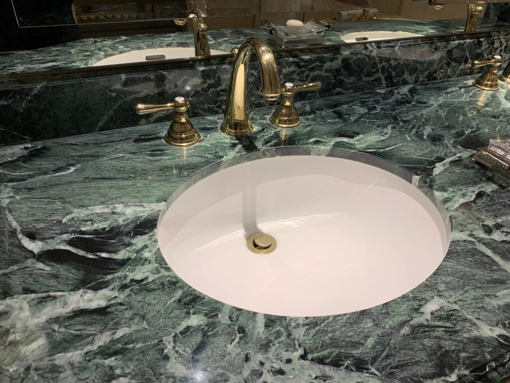 A green marble counter top with a round sink with a gold faucet 