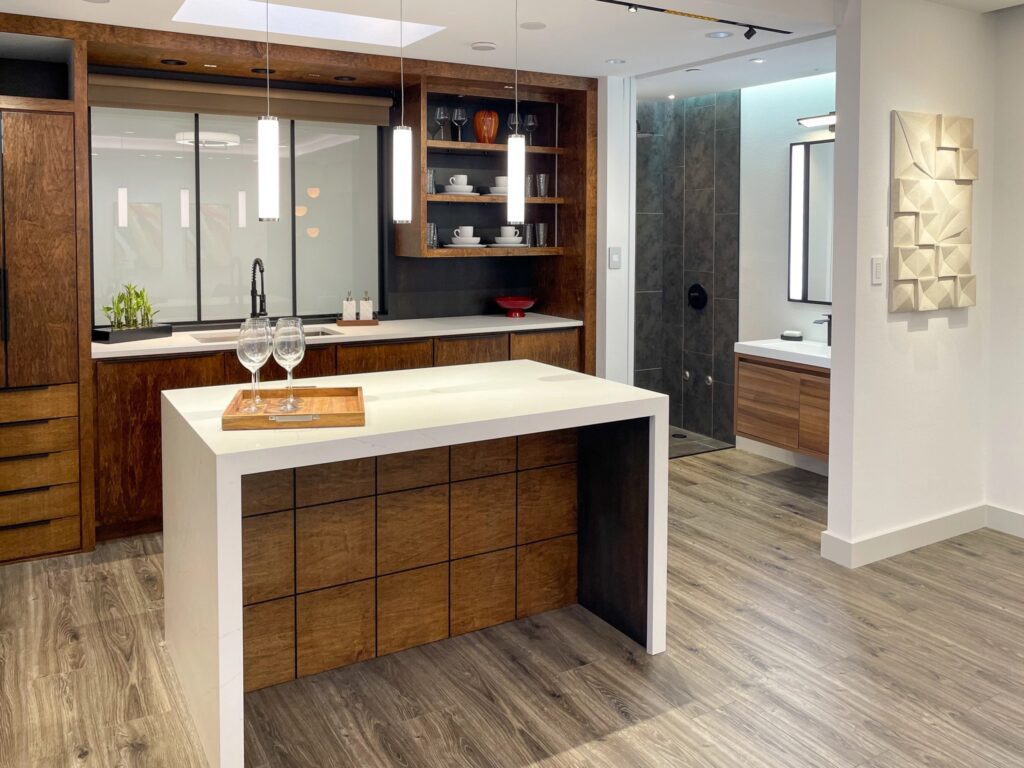Wide shot of a kitchenette and island. The island is white with room for chairs for people to sit at. The cabinets for the kitchenette are dark brown.