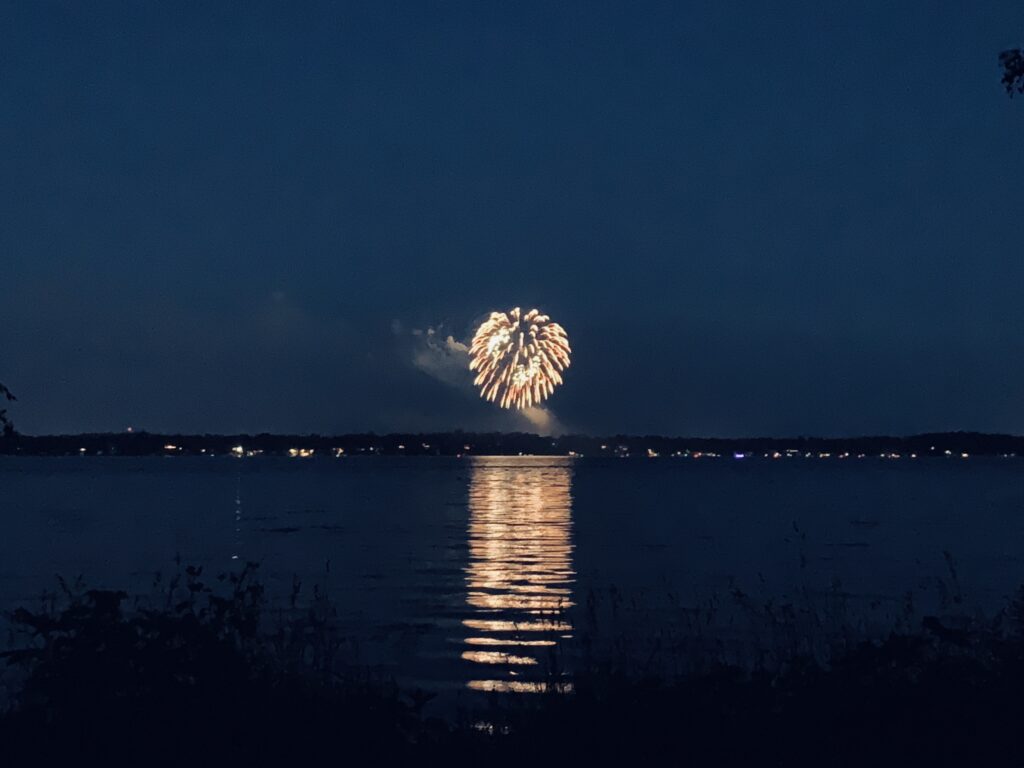 Photograph of an exploding firework as seen from across a lake.