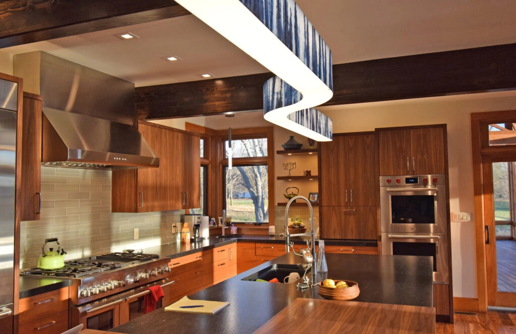 A modern kitchen with wooden cabinets and black countertops. There is a swoosh sculpture light above the kitchen island