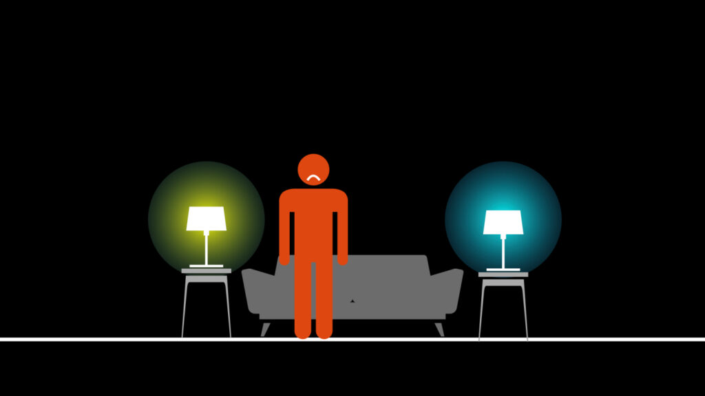An illustration of a red person with a frown standing in front of a couch with a yellow light on an end table on the left and a blue light on an end table on the right.