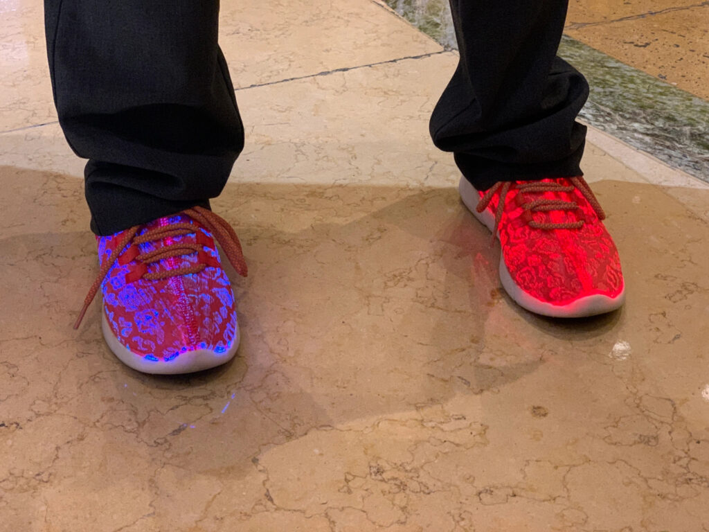 A person wearing shoes that are lit from the inside. The left shoe is neon blue and orange and the right is neon orange.