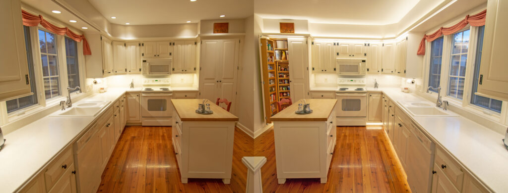 A mirror shot of a kitchen with white cabinets, walls, and countertops, and nice hardwood floor. The kitchen on the left has poorer lighting than the kitchen on the right, showing a BEFORE and AFTER effect in the difference.
