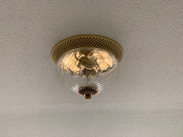 An overhead light that has a gold base and tip, and a textured clear glass globe