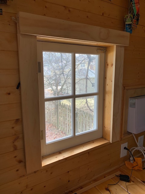 A window with four panes in a wooden wall viewing the outdoors on a sunny day
