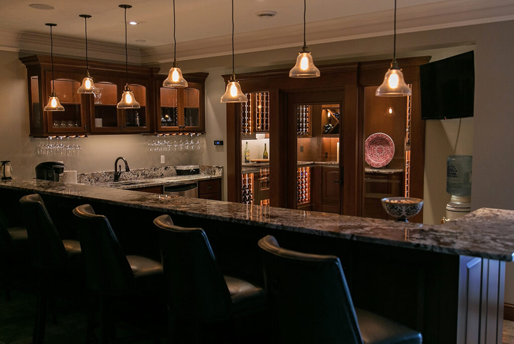 A photograph of a kitchen with a long countertop for diners. The only lights on are the pendants over the counter, the cabinet lights, and the ceiling lights.