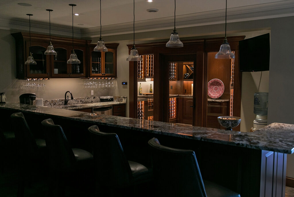 A photograph of a kitchen with a long countertop for diners. The only lights on are the ones underneath the cabinets.