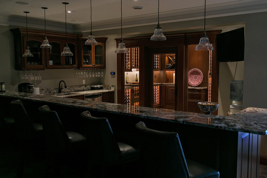 A photograph of a kitchen with a long countertop for diners. All is dark save for the lights illuminating the items in the display cabinet.