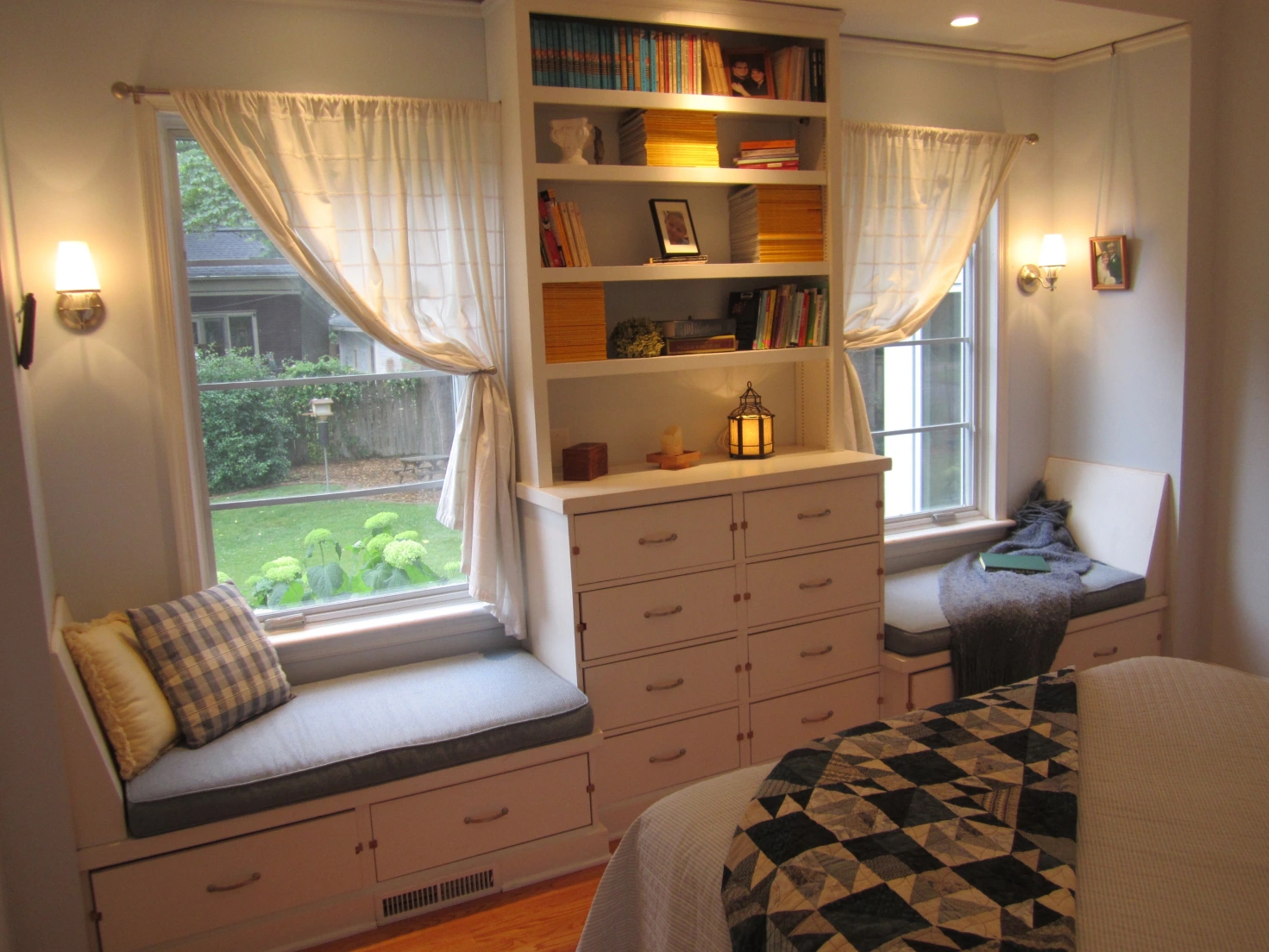 A bedroom with the bed off to the left, the right shows two windows framed with built in drawers and shelves and window seats