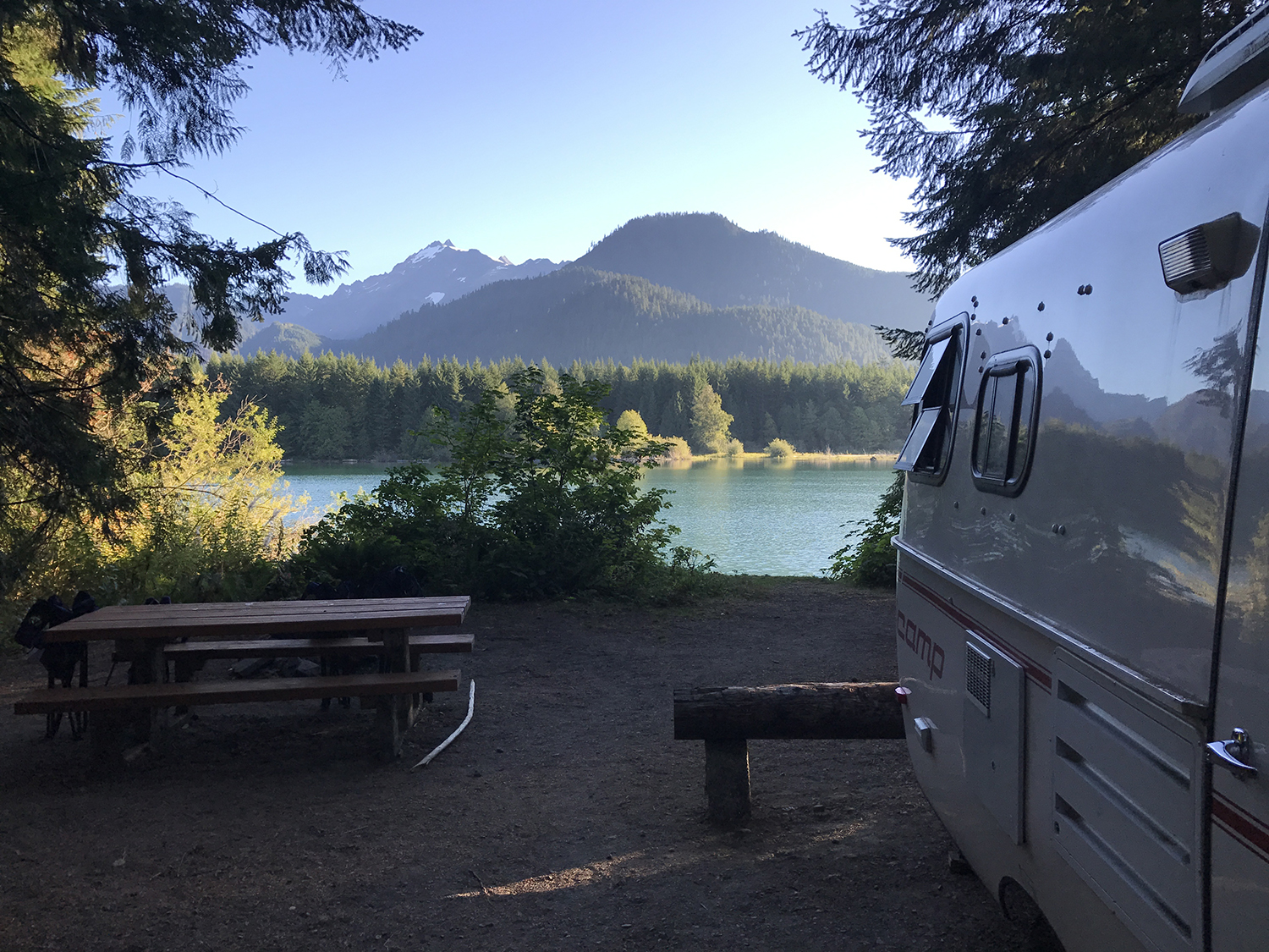 A photograph of a camper at a campsite on a lake. Across the lake is a mountain. The scene looks very pleasant.